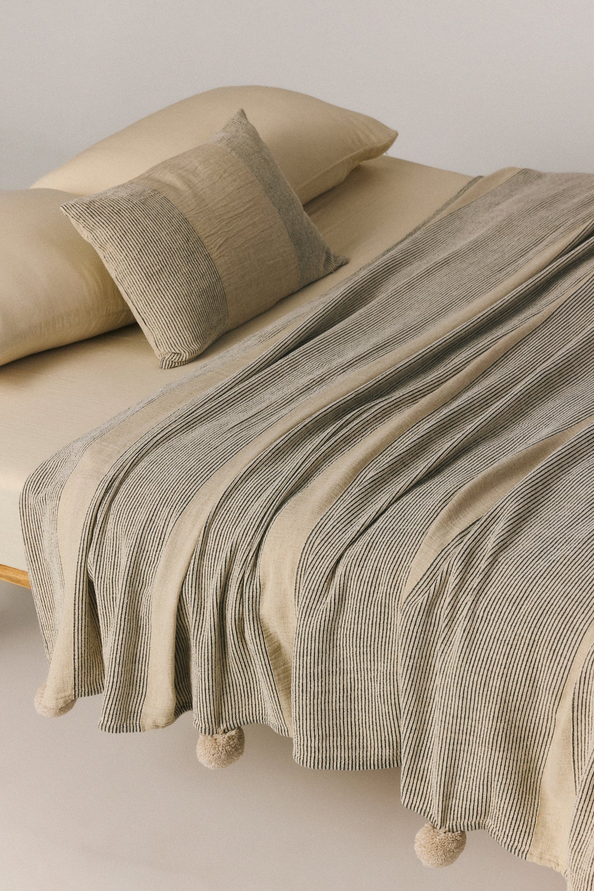 Korfu linen coverlet with pompom trim detail in black, draped over bed